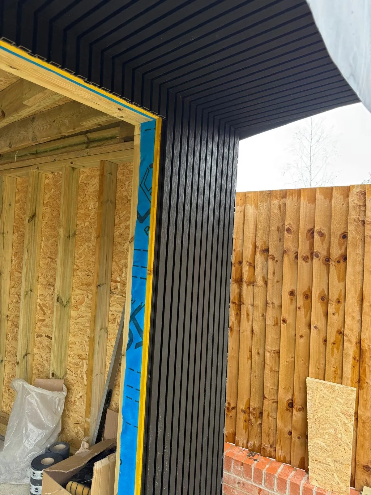 Black cladding being fitted to the corner of a garden room