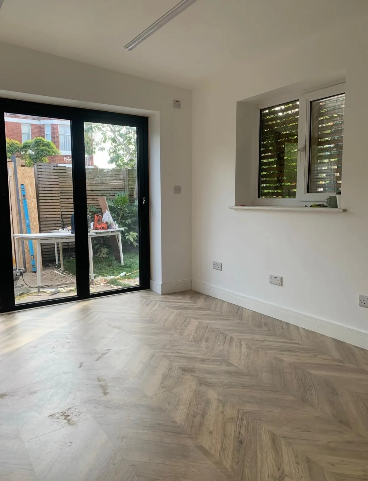 Bright finished garden room interior with herringbone floor and black-framed doors