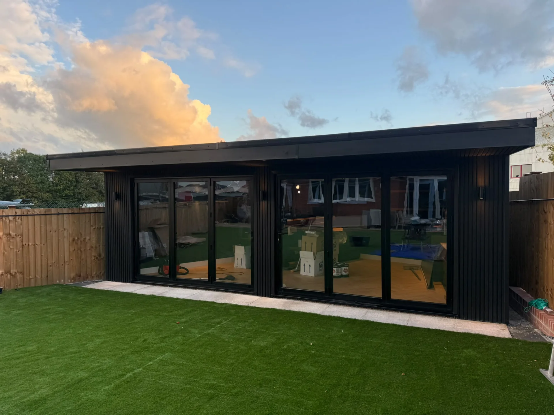 Black-clad garden room with illuminated overhang and glazed doors viewed from the lawn