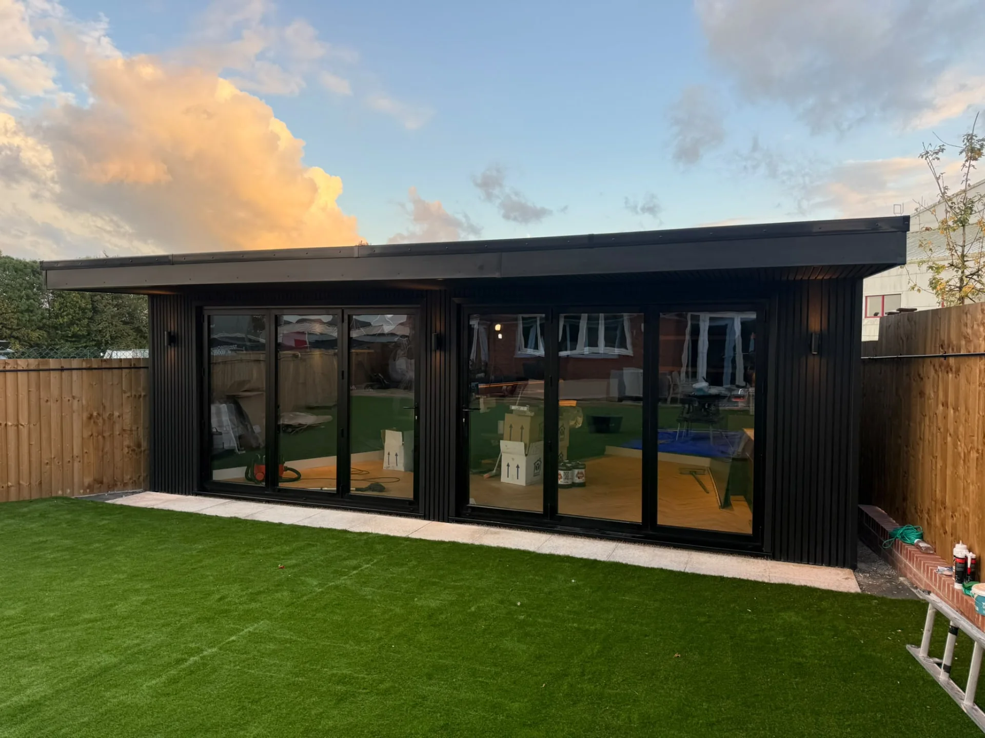 Black-clad garden room with two sets of glazed doors and a deep roof overhang at sunset