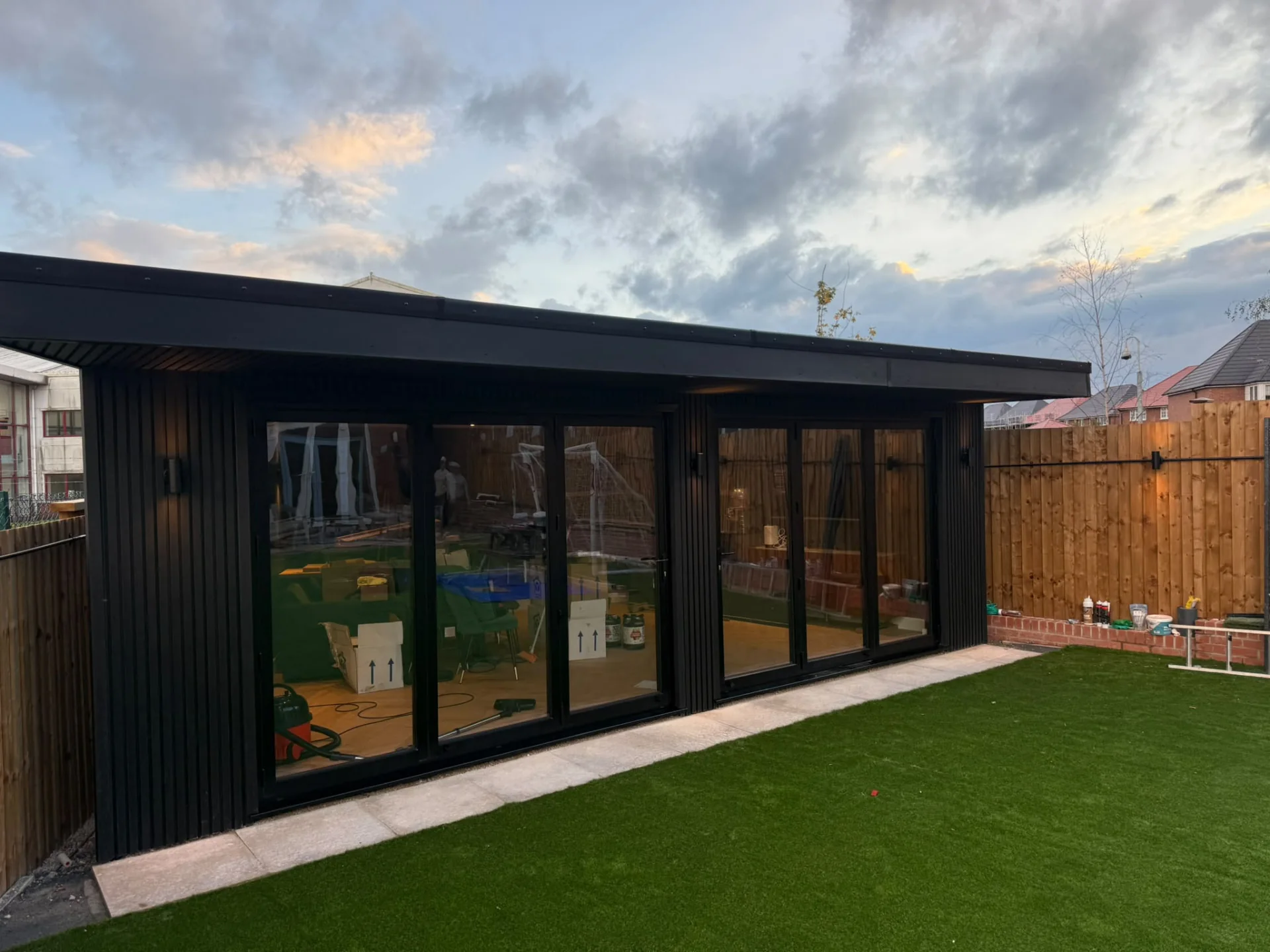 Black-clad garden room beside a lawn and timber boundary fence